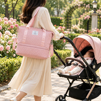 Sac à langer extensible rose porté à l’épaule par une femme près d’une poussette dans un parc fleuri