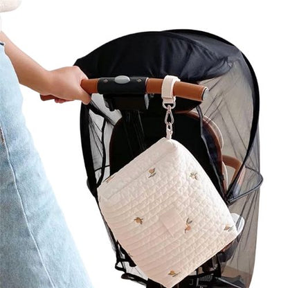 Sac a langer feuillage accroche a une poussette noire, vue de cote avec main d’adulte