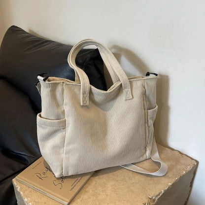 Sac à langer beige en tissu côtelé posé sur un canapé, format compact et pratique