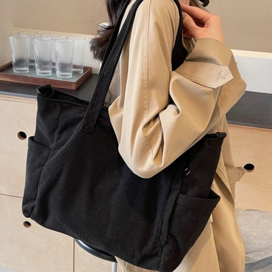 Sac à langer noir en tissu côtelé porté à l’épaule, style sobre et moderne pour parents