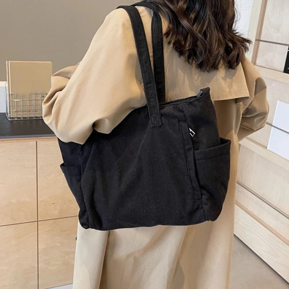 Sac à langer noir porté à l’épaule par une femme en manteau beige, design côtelé pratique