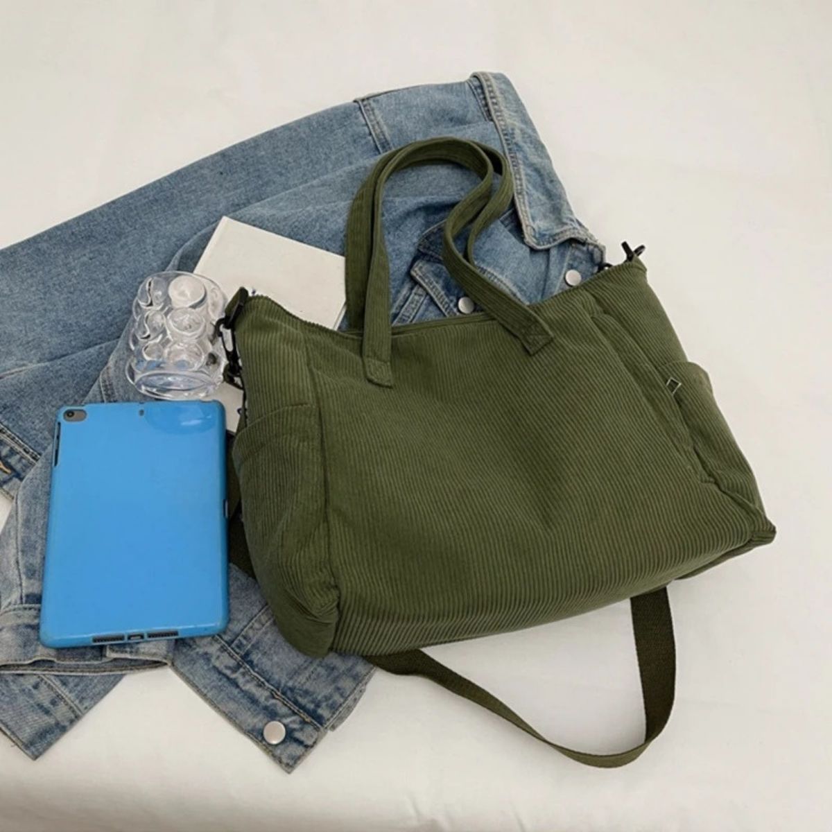 Sac à langer vert sur un jean et une tablette bleue, style moderne et pratique