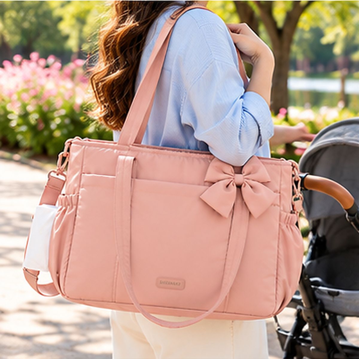 Sac à langer rose pâle avec grand nœud décoratif et deux anses, porté à l'épaule près d'une poussette