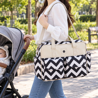 Sac à langer multipoches motif Chevron noir et blanc porté à l’épaule près d’une poussette