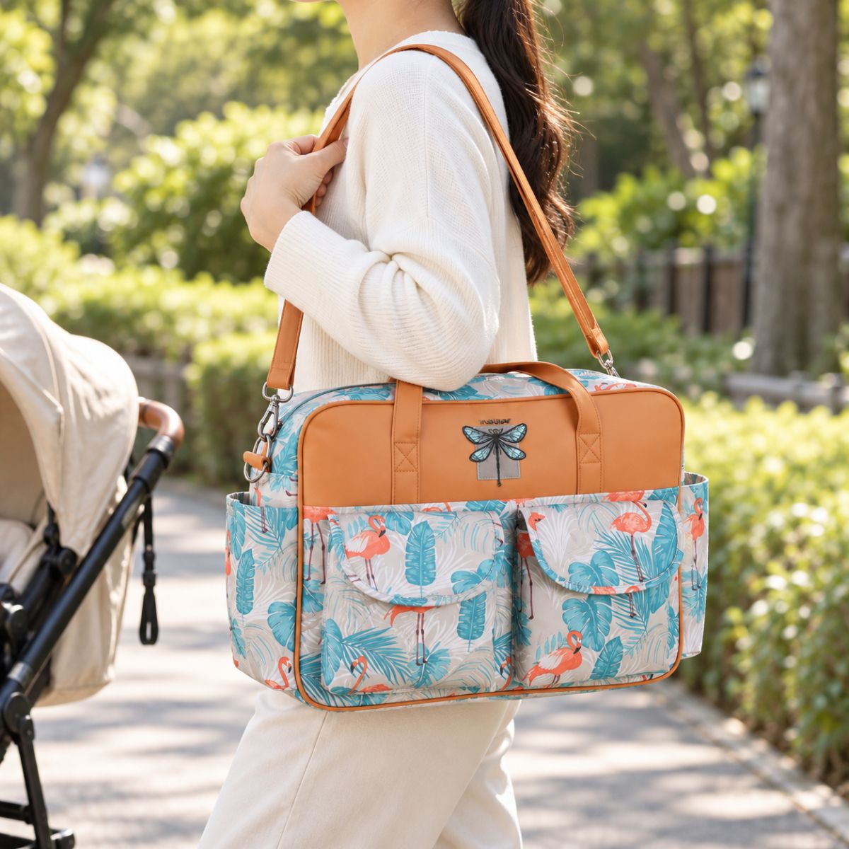 Sac à langer multipoches motif Flamant rose porté à l’épaule près d’une poussette