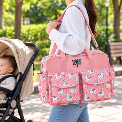 Sac à langer multipoches motif Lama rose porté à l’épaule près d’une poussette