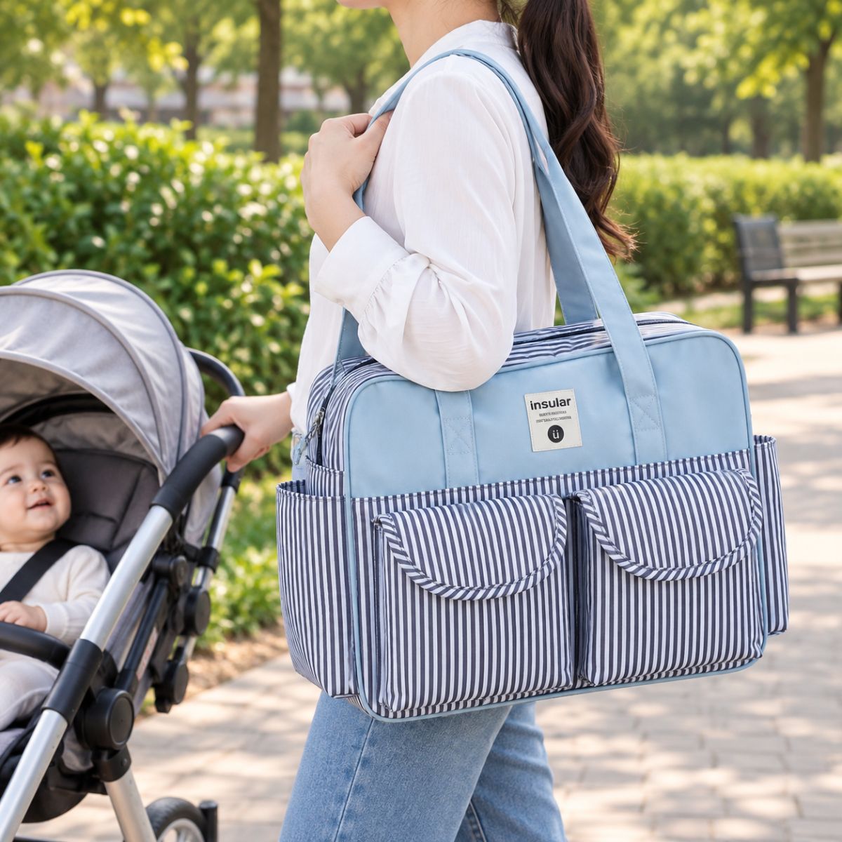 Sac à langer multipoches motif Rayures Bleues porté à l’épaule près d’une poussette
