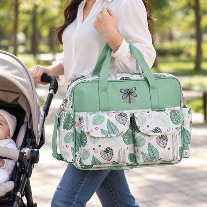 Sac à langer multipoches motif Tropical vert porté à la main près d’une poussette