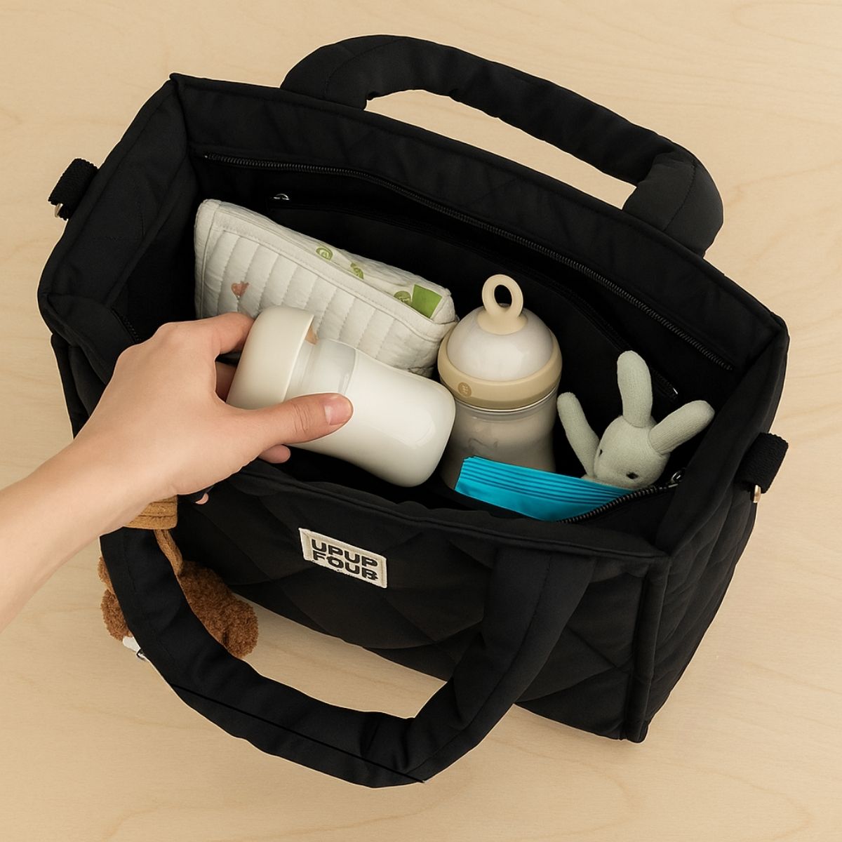 Vue interieure d’un sac a langer noir contenant biberon, doudou et accessoires pour bebe