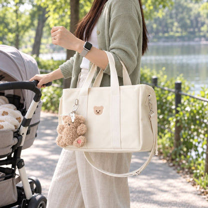Sac à langer ourson finition Beige, porté au bras près d'une poussette dans un parc, avec anses claires et bandoulière visible