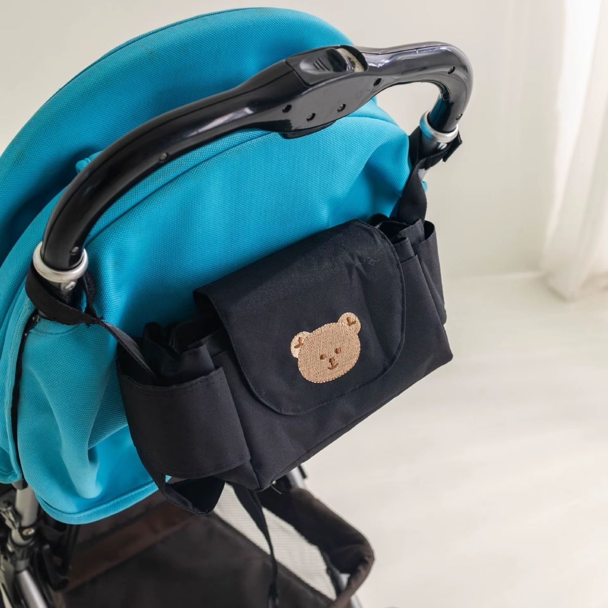 Sac a langer pour poussette motif ours beige attaché à une poussette bleue pliable