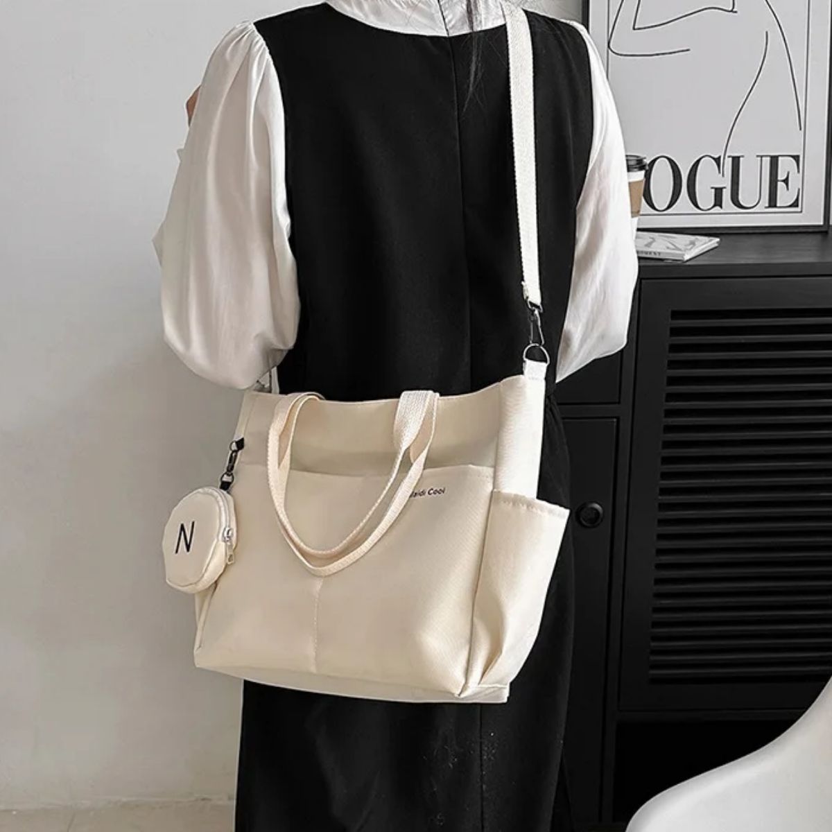 Sac a langer beige vu de dos, porté en bandoulière par une maman en robe noire et blanche