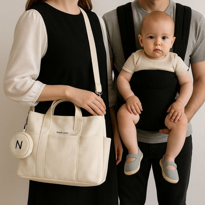 Sac a langer beige porté à la main par une maman, bébé en porte-bébé noir tenu par le papa