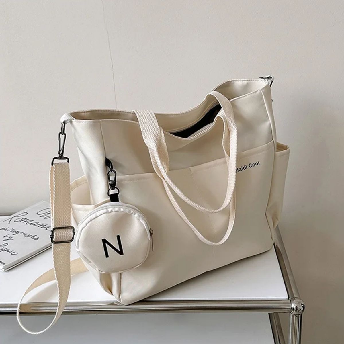 Sac a langer beige posé sur une table métallique, bandoulière ajustable et pochette ronde assortie