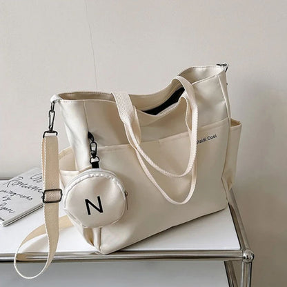 Sac a langer beige posé sur une table métallique, bandoulière ajustable et pochette ronde assortie