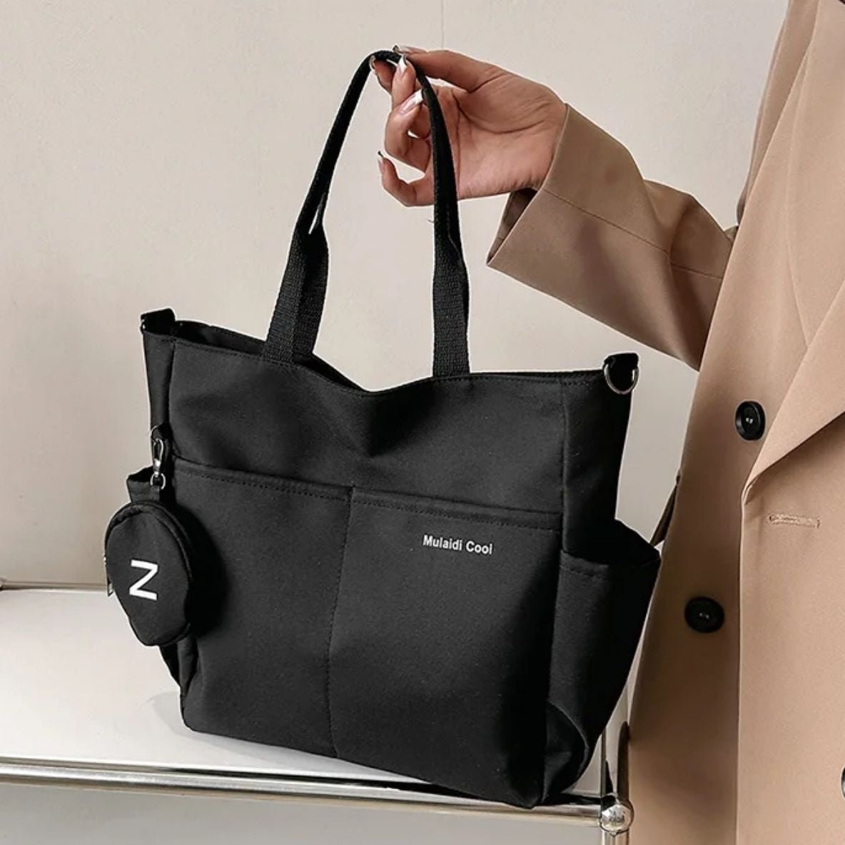 Sac a langer noir tenu à la main, design sobre posé sur une table blanche