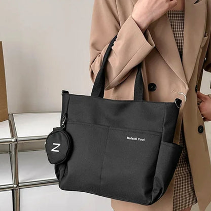 Sac a langer noir porté à l’épaule par une maman en veste beige, format tote pratique