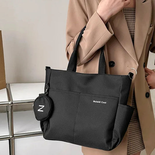 Sac a langer noir porté à l’épaule par une maman en veste beige, format tote pratique