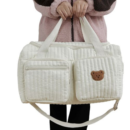sac a langer creme avec un ours brode porte a la main par un adulte