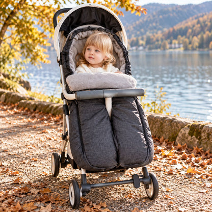 Sac de couchage pour poussette gris anthracite à jambes séparées avec bébé lors d’une promenade au bord d’un lac en automne