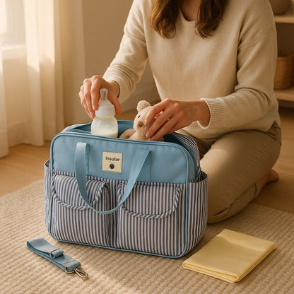 Sac de maternité Rayures Bleues ouvert sur le sol, biberon et doudou dans la poche principale.