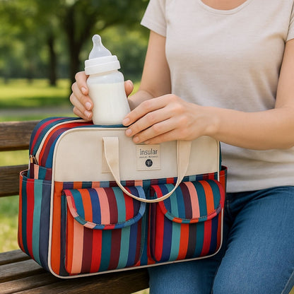 Sac de maternité Rayures Colorées posé sur un banc, une maman tient un biberon prêt à l’emploi