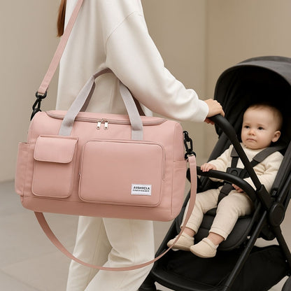 Sac maternité rose foncé porté en bandoulière par une femme à côté d’une poussette avec bébé