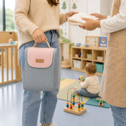Sac pour deux biberons rose et gris avec poignée intégrée, tenu à la main dans une crèche