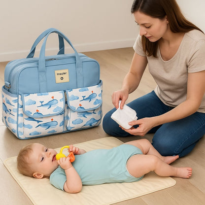 Sac pour la maternité baleine bleue posé au sol près d’une maman changeant son bébé